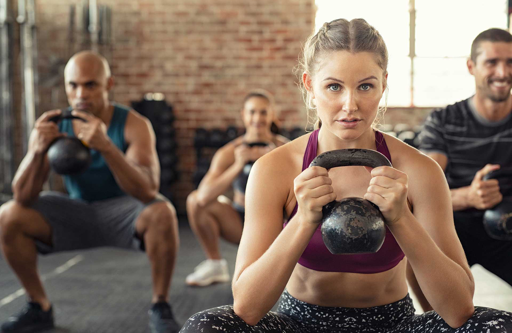 a group of 4 people squatting with kettlebells