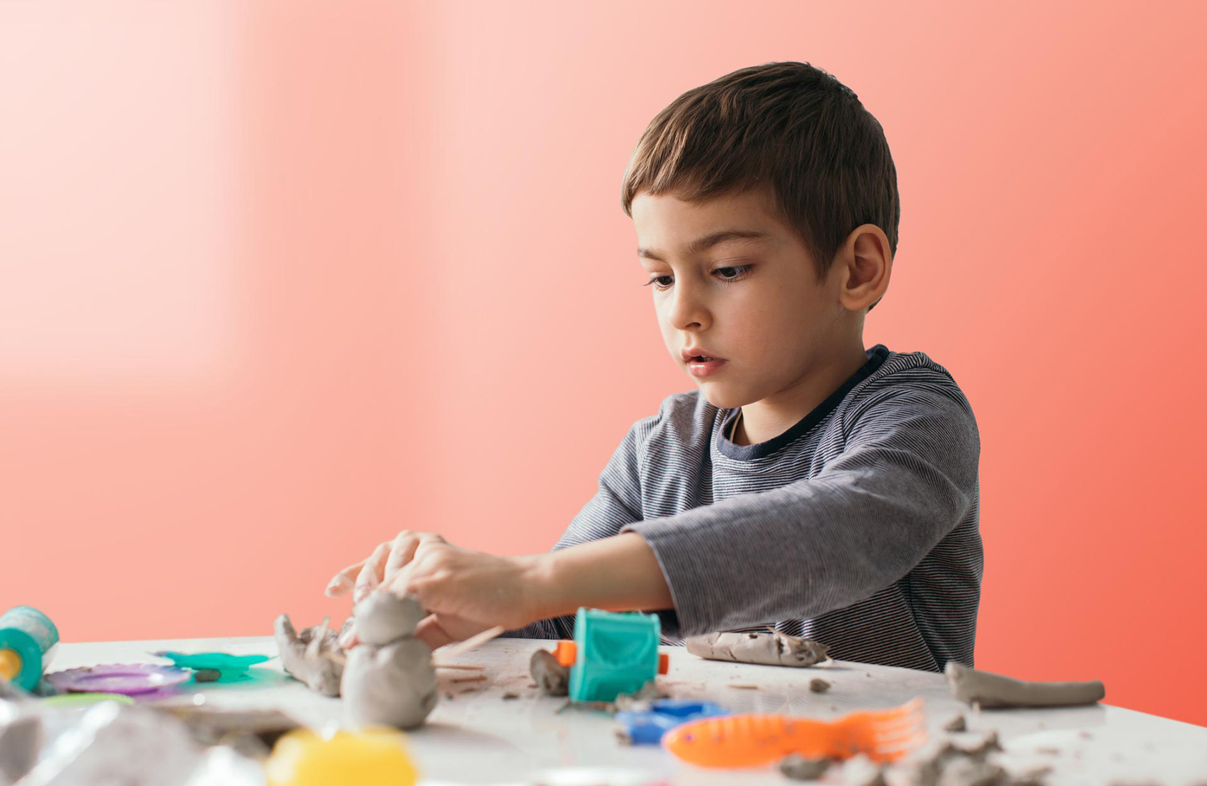 a young boy sitting at the table playing with clay