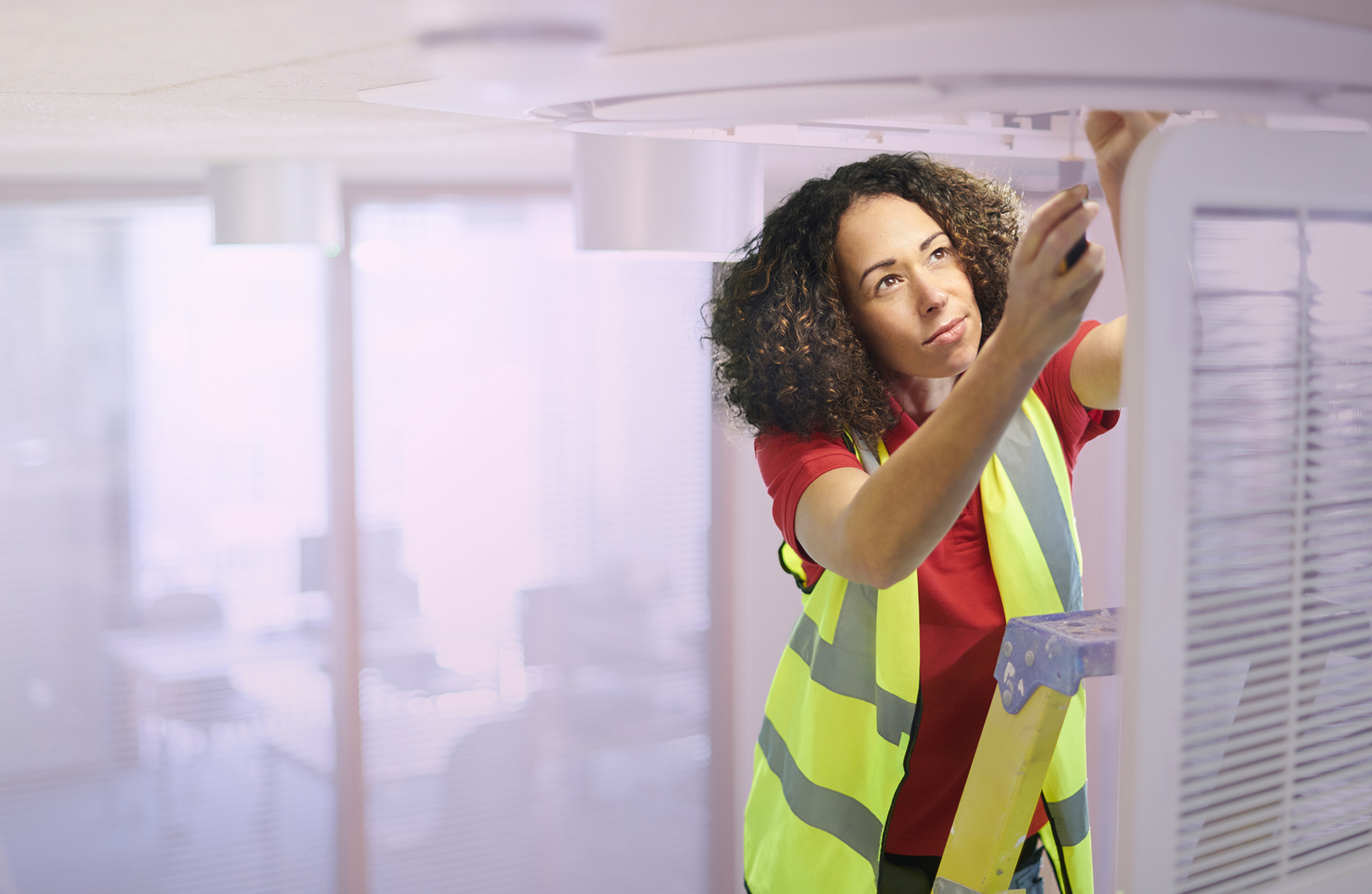 a young woman holding a skewdriver fixing a ventalation system