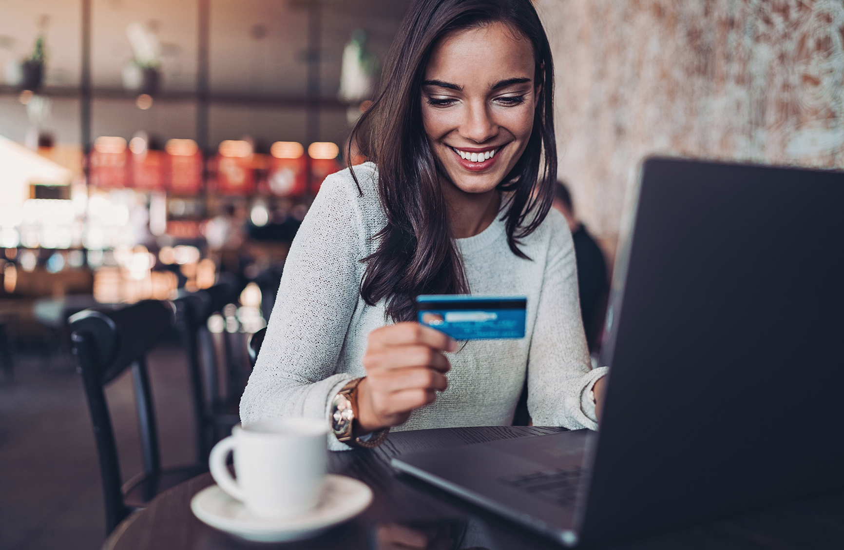Smiling businesswoman holding a credit card and using laptop in a restaurant